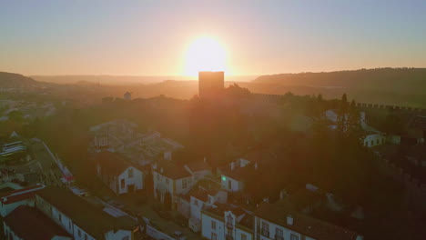 sunset highlighting old town rooftops and ancient wall. silhouette obidos castle
