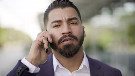 hombre de negocios serio en chaqueta de traje hablando por teléfono inteligente al aire libre