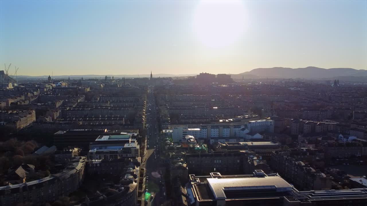 Drone footage of Edinburgh’s iconic skyline at sunset, showcasing historic rooftops and distant hills. The clip captures the autumn landscape with long shadows and warm lighting from the setting sun.