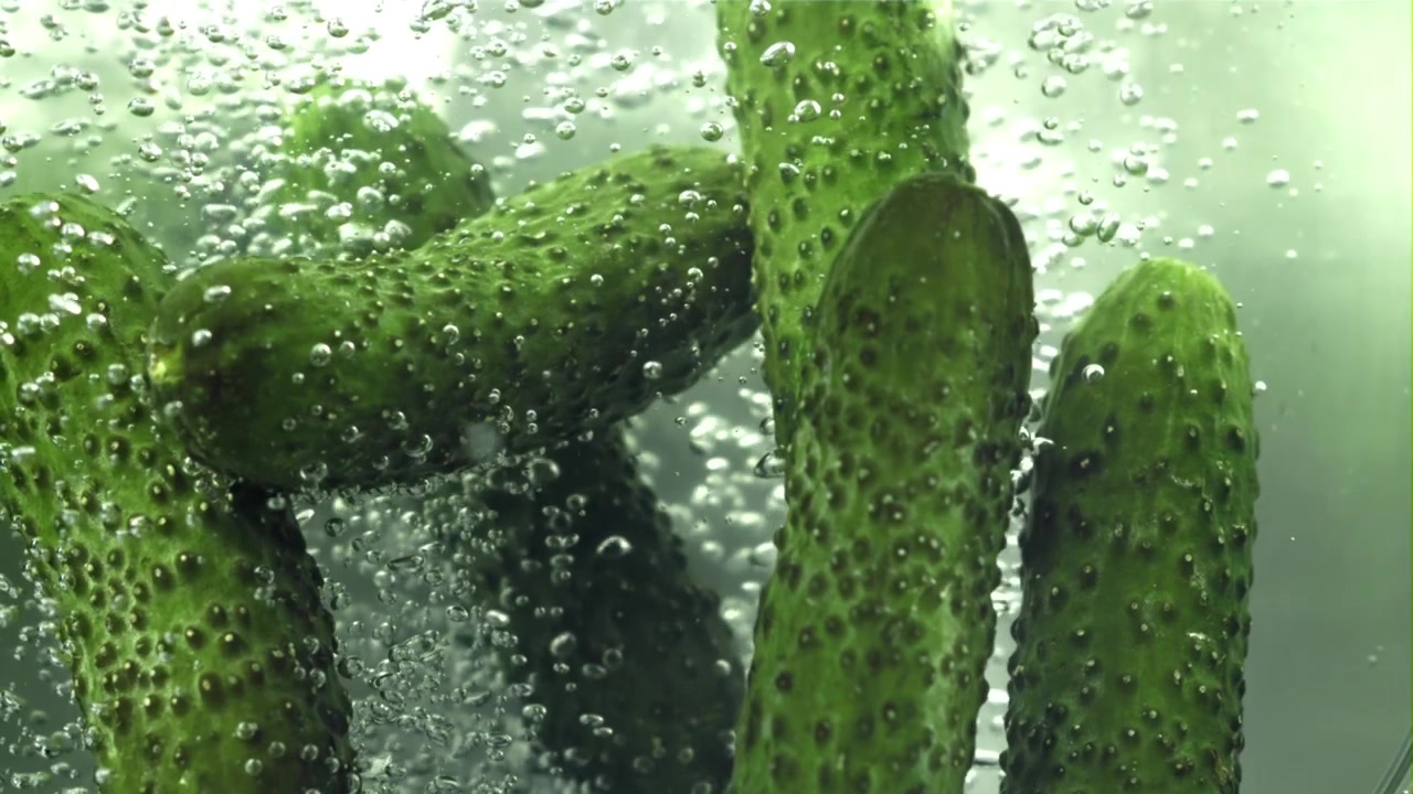 Färska gröna gurkor nedsänkta i bubblande vatten