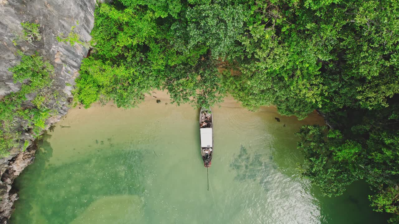 vista aérea de arriba hacia abajo de un barco de cola larga a lo largo de una playa con aguas turquesas y acantilados de piedra caliza en blue's hong, ko roy, tailandia