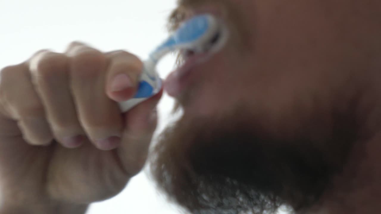 Close up profile view shot of a bearded man brushing teeth against white background