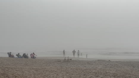 Kinder-Schwimmen-Und-Spielen-Im-Meer-An-Einem-Nebligen-Morgen-Am-Strand,-Während-Die-Eltern-Zusehen