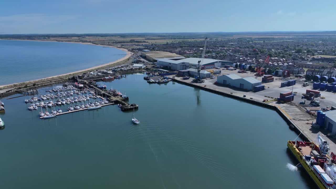 Drone clip over industrial area with large boat and many smaller sailing boats moored in harbour