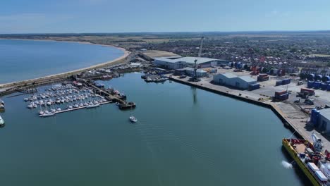 drone clip over industrial area with large boat and many smaller sailing boats moored in harbour