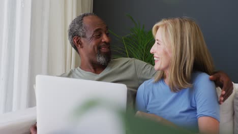 Mixed-race-senior-couple-using-laptop-while-sitting-on-the-couch-at-home