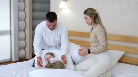 toddler beloved by their parents lies in the pillows. mom and dad play with their adorable toddler son in the bedroom.