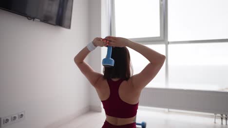 Sporty-girl-exercising-with-dumbbells-at-home,-back-view