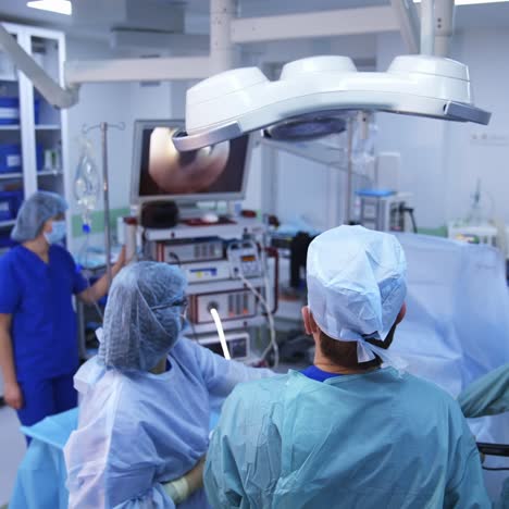 surgery in modern operating theater. doctors in medical uniform looking on the screen with operative process. high-tech operation. back view