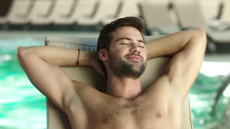 Closeup-man-relaxing-by-pool-at-luxury-spa.-Man-sleeping-poolside-on-lounger