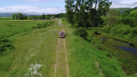 red truck traveling on a trail between greenfields at summertime