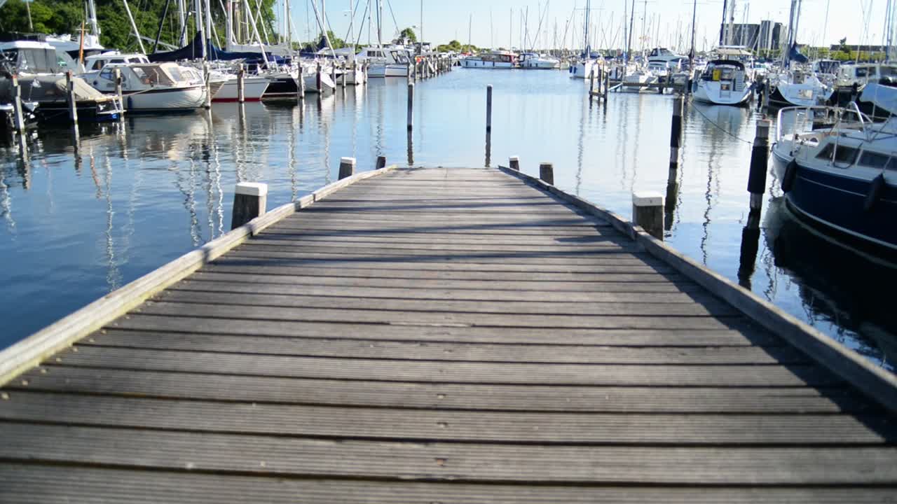 A small harbour with a wooden pier and numerous sailboats at sunset