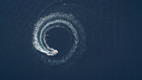 aerial view of a boat driving in circles forming waves around in greece.