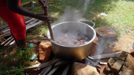 african woman stirring big pot of meat on-top of wood fire