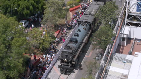 steam train rolling through city center with large crowd of spectators