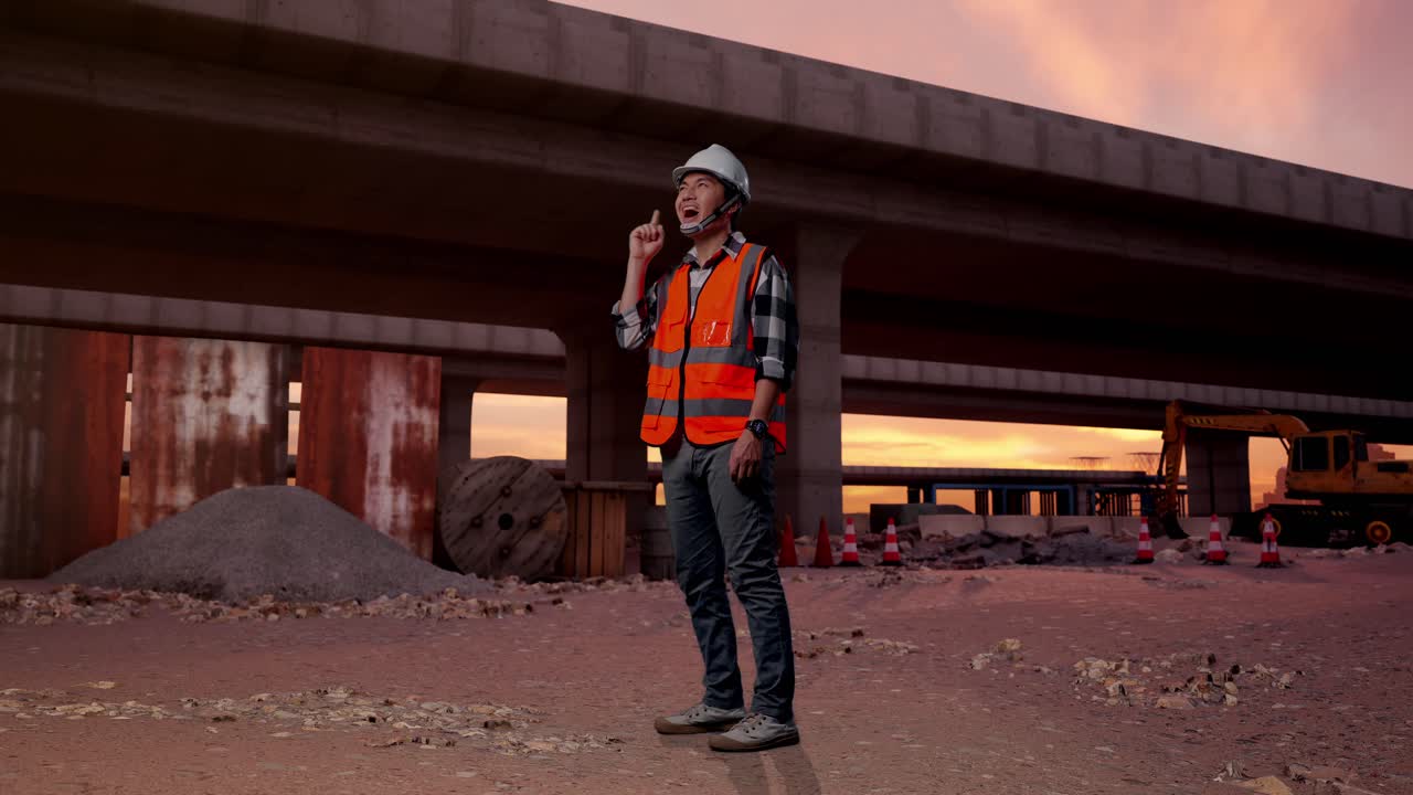 Full Body Side View Of Asian Male Engineer With Safety Helmet Thinking And Looking Around Then Raising His Index Finger While Standing At The Site of Highway Construction