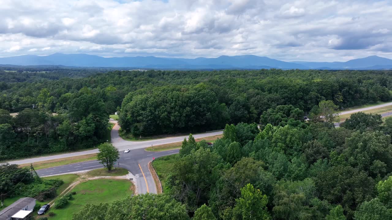 Aerial approaching shot of rural America. Highway with traffic on cloudy day. Suburb area with forest and woodland in summer. Driving cars on interstate road