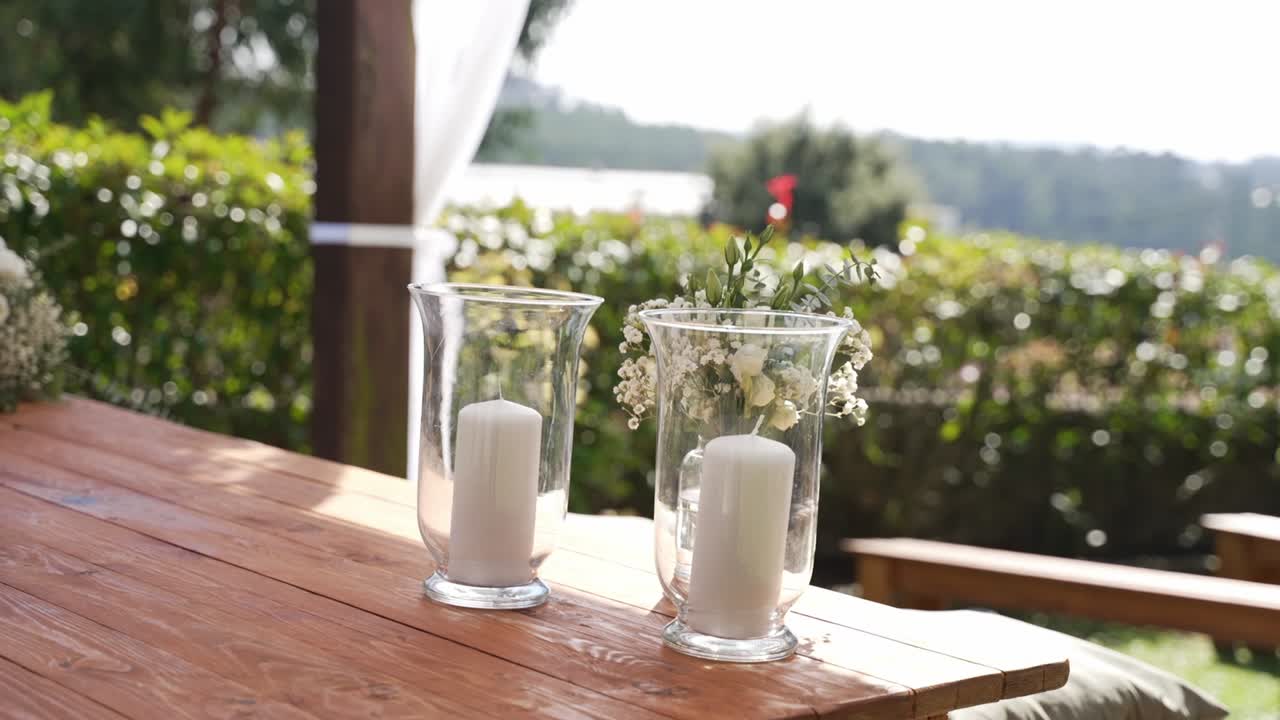 Two glass candle holders with white candles on wooden table outdoors