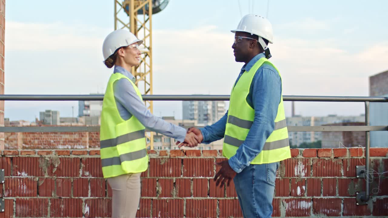 hombre y mujer multiétnicos con cascos de pie en el sitio de construcción, hablando y estrechando la mano. encuentro entre constructor y arquitecto. al aire libre.