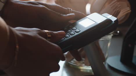 close up hands using credit card machine typing password customer making payment spending money in cafe