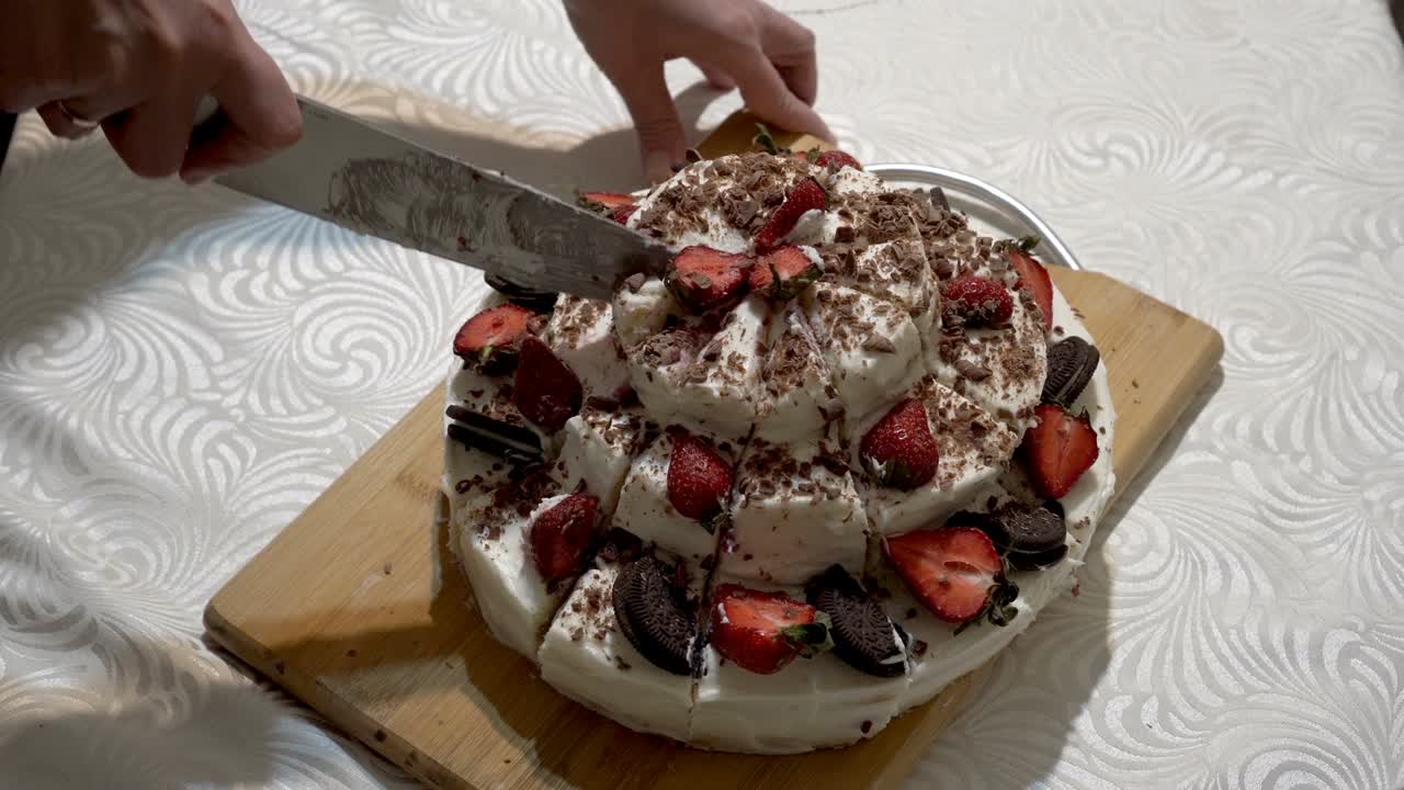 여성의 손이 큰 주방 칼로 나무판에 아름다운 집에서 만든 딸기 케이크를 똑같은 조각으로 잘라내는 클로즈업.