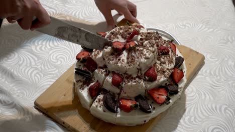 close-up of women's hands cutting a beautiful homemade strawberry cake into identical pieces on a wooden board with a large kitchen knife. the concept of a home holiday. faceless. top view. 4k.