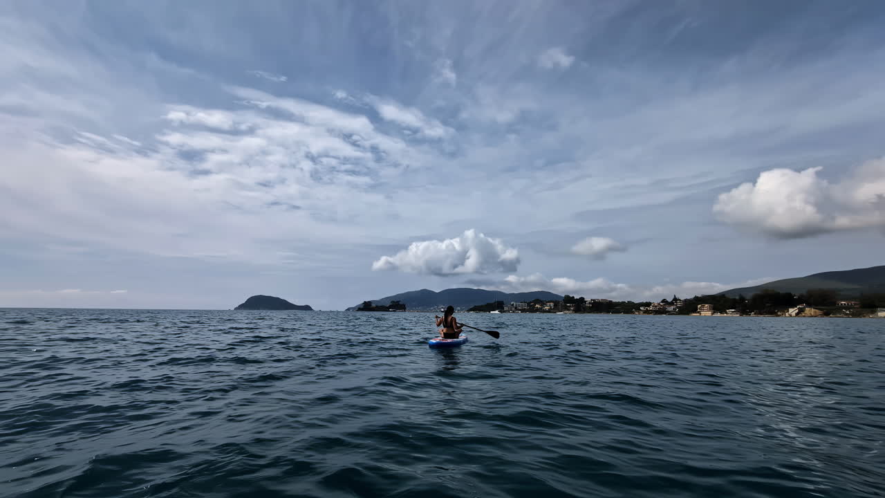 A person paddling on a blue board in the ocean under a cloudy sky