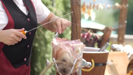 female slicing prosciutto on table outdoors, detail shot of woman cutting raw meat