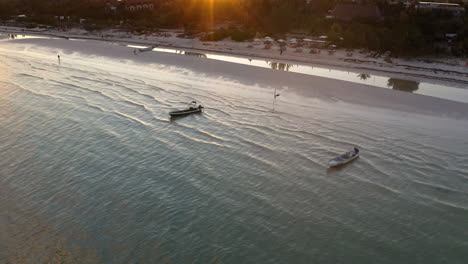 Motorboats-anchored-by-sandy-beach-at-sunset,-waves-washing-upon-shore