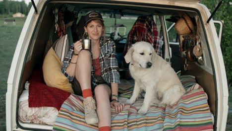 portrait of happy woman and dog in van with lifted rear door