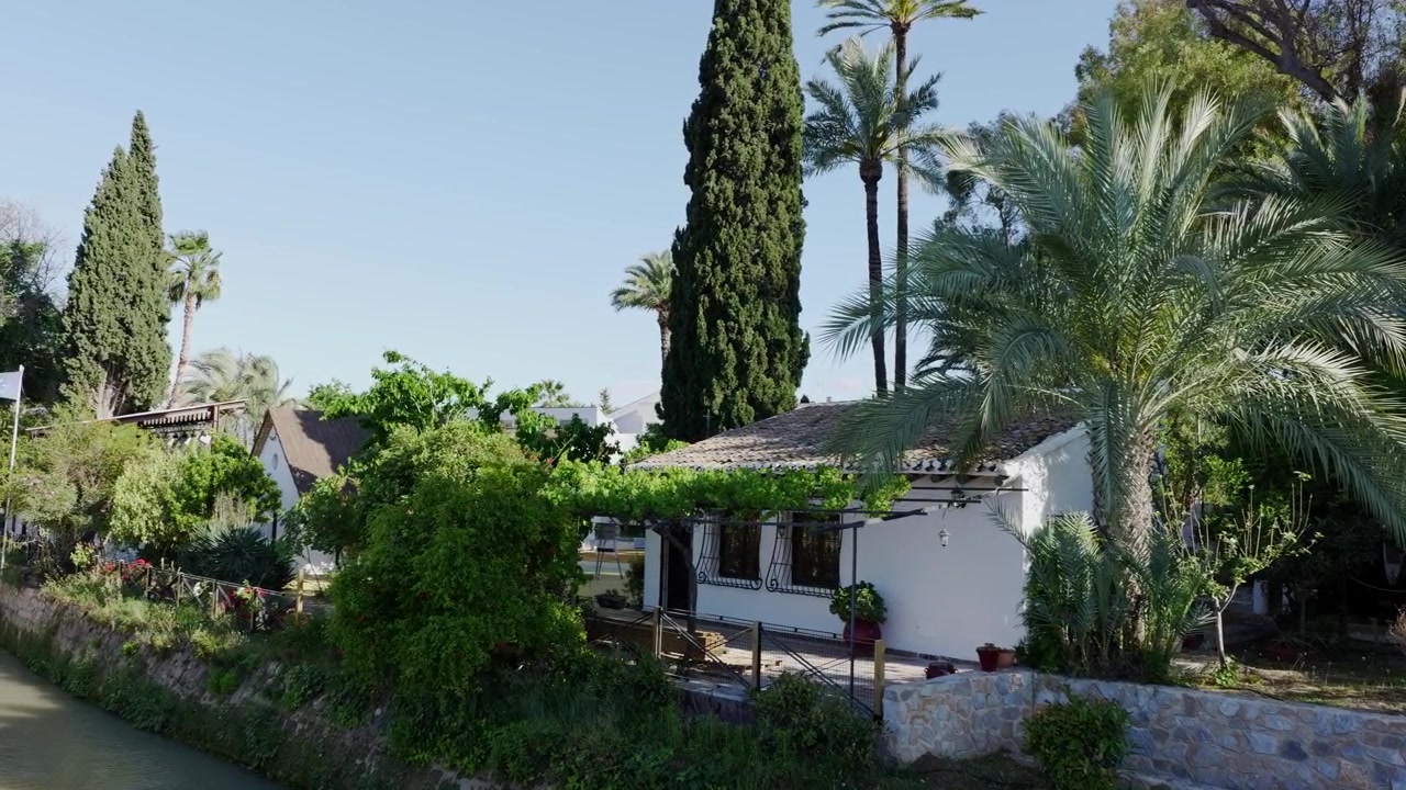 Casa tradizionale imbiancata a calce presso il Museo de la Huerta ad Alcantarilla, circondata da palme da dattero, alti cipressi, una lussureggiante vegetazione da giardino, un muro di pietra e un canale di irrigazione tradizionale