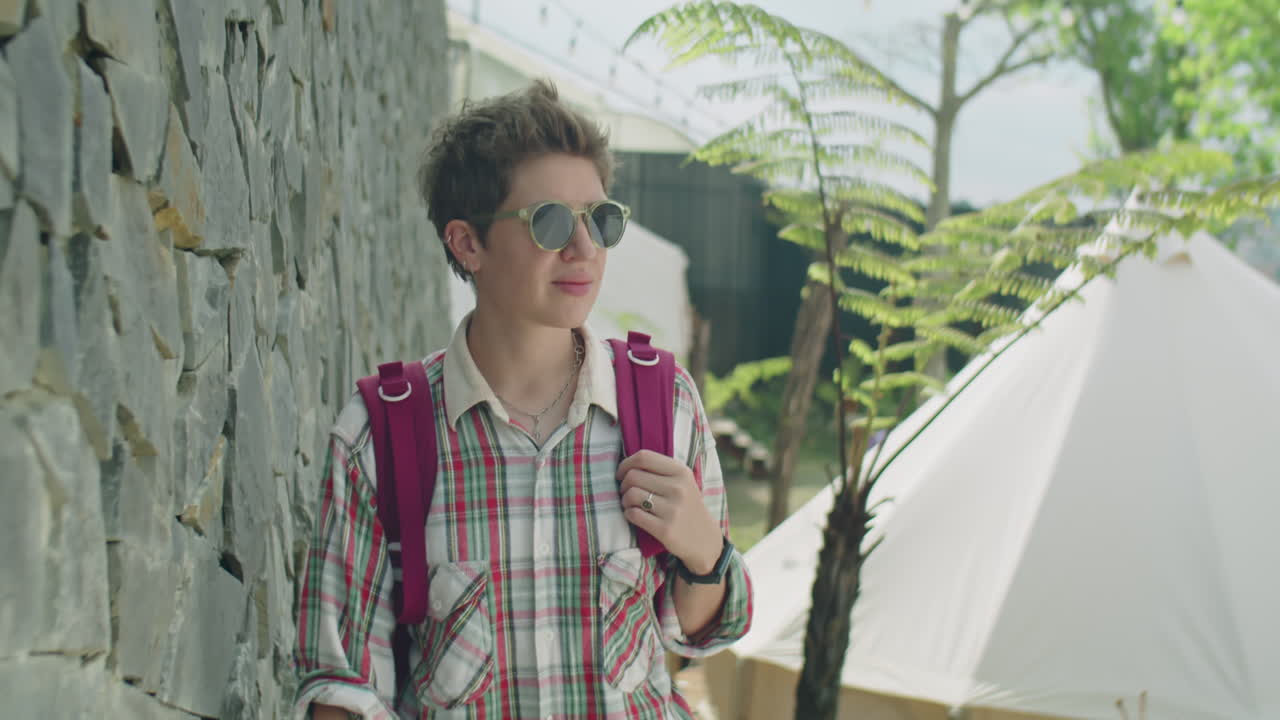 Woman Walking with Backpack Along Stone Wall at Glampsite