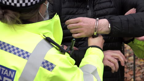 a police officer holds on to the handcuffs being used to restrain an arrestee