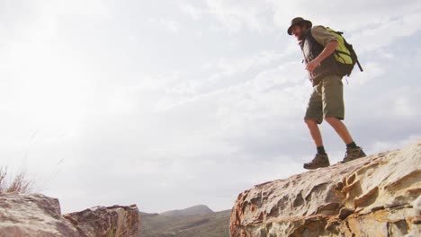 sobreviviente caucásico barbudo con mochila saltando a través de un barranco de montaña rocosa en el desierto