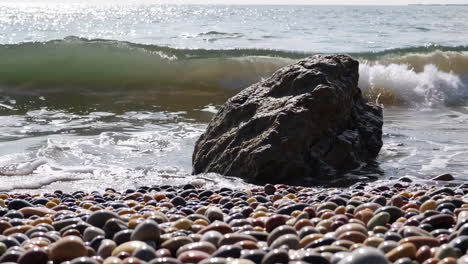ocean waves crashing on pebbly beach with a large rock