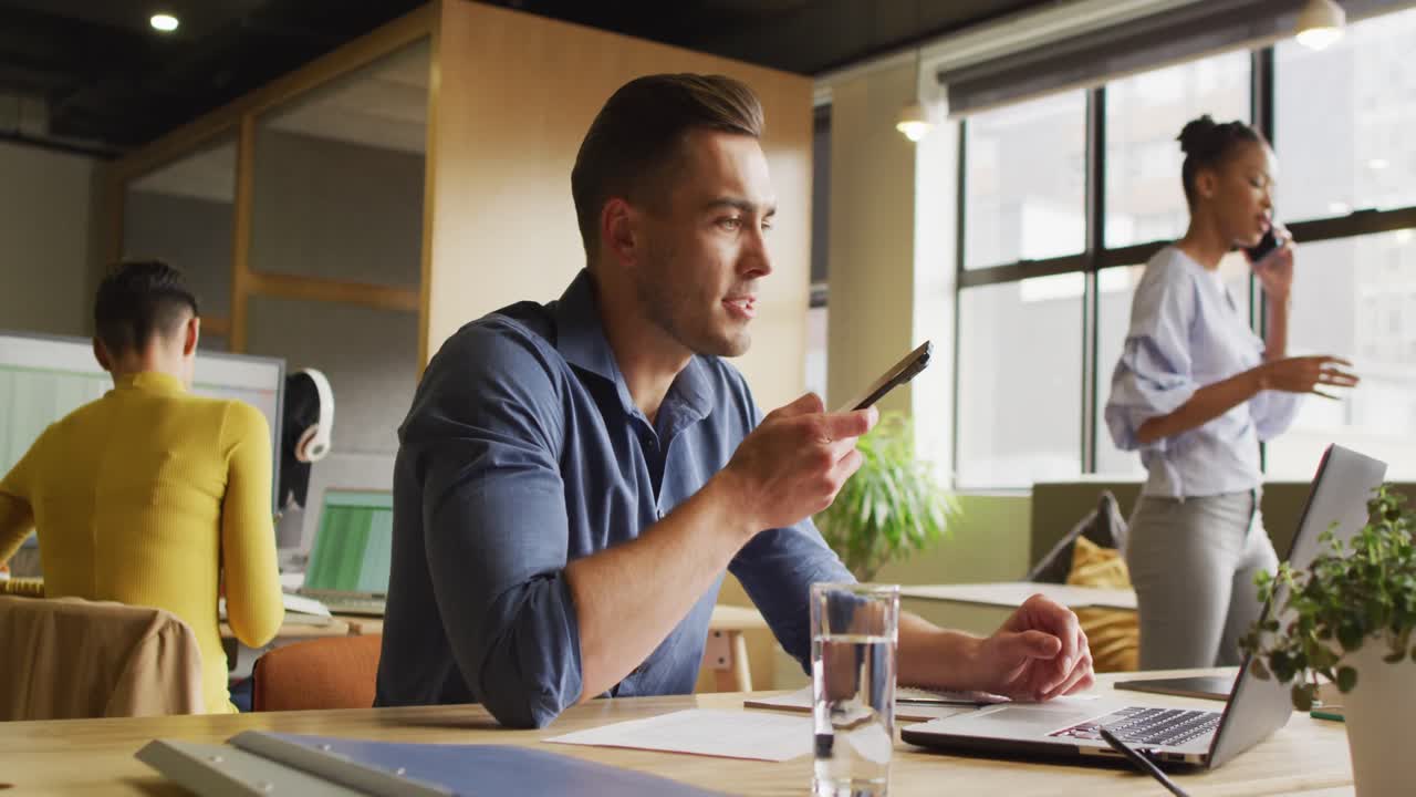 feliz hombre de negocios caucásico sentado a la mesa y usando un teléfono inteligente en la oficina