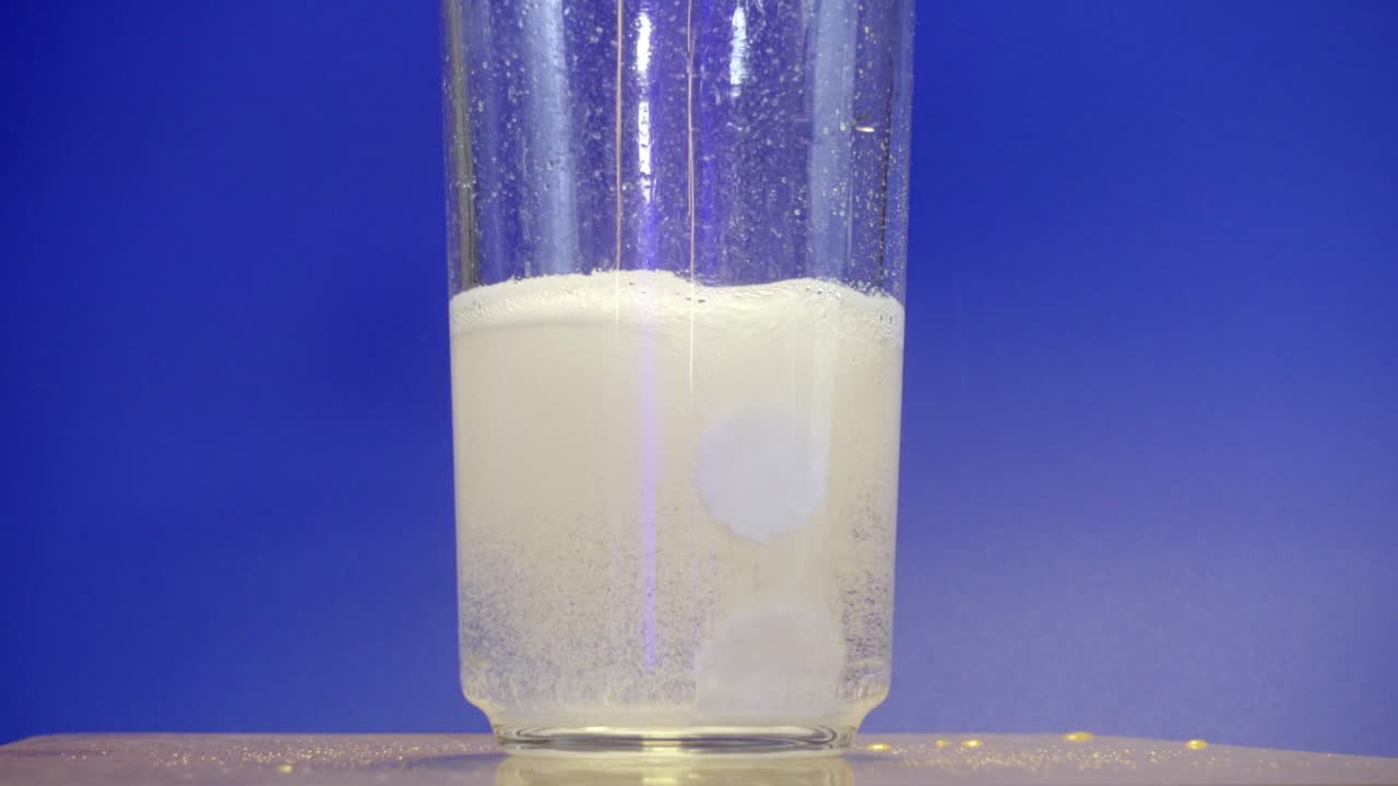 A transparent glass rotates slowly showing a fizzy drink with bubbles against a blue background