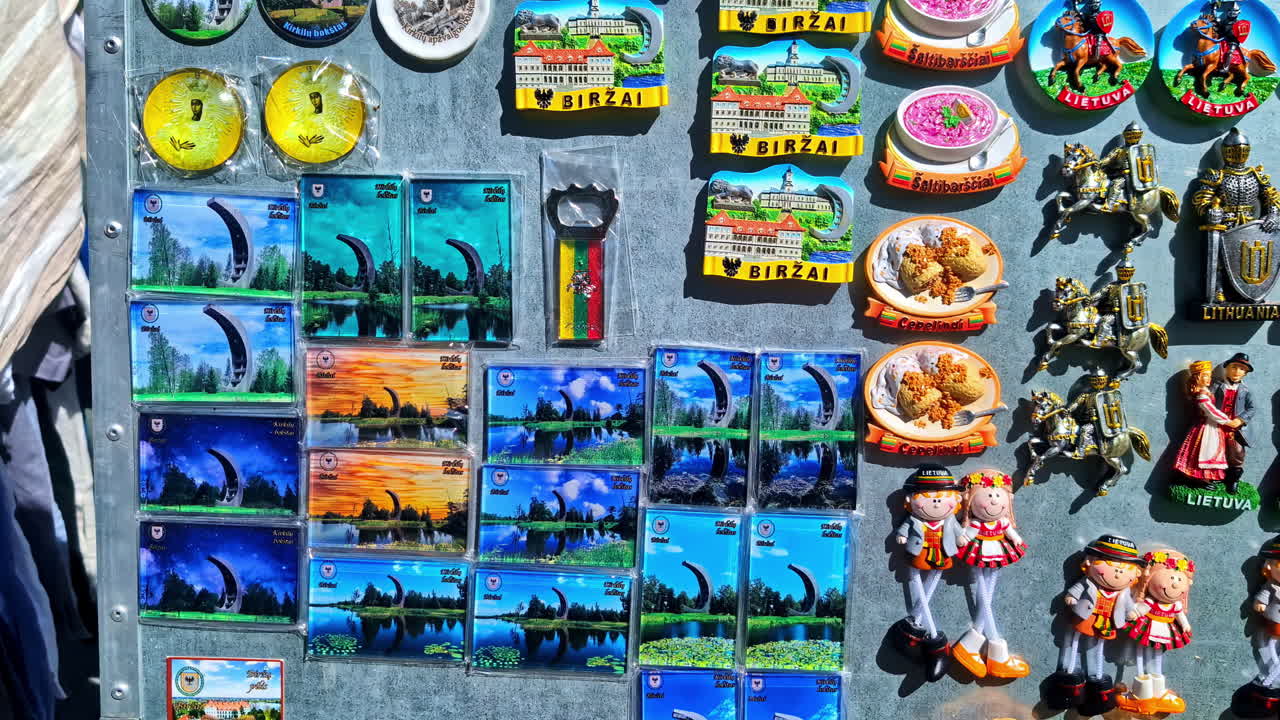 A vibrant collection of Birzai, Lithuania souvenir magnets featuring landmarks, foods, and traditional costumes arranged on a metal display at a market