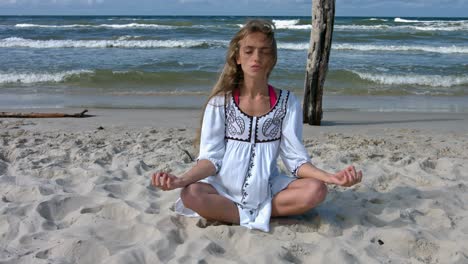 young beautiful woman trains breath practicing yoga and meditation on the sea beach on a warm summer sunny day