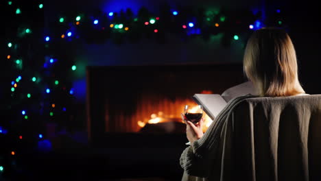 a woman reads a book by the fireplace next to the decorations for christmas and new year