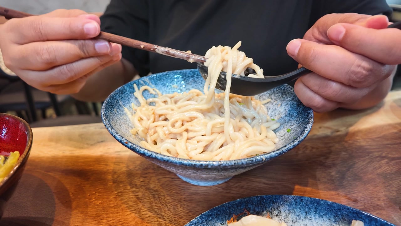 Primo piano di una persona che usa bacchette e un cucchiaio per sollevare i noodles taiwanesi Ma Jiang Mian