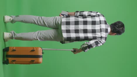 full body back view of a male traveler with luggage holding passport and and looking around while standing in the green screen background studio