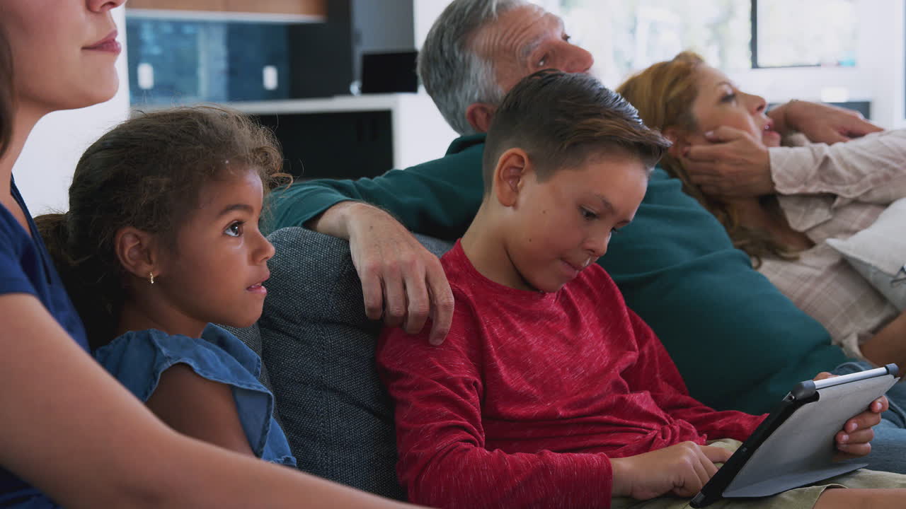 Spansktalende familie i flere generationer slapper af på sofaen, mens barnebarnet leger med en digital tablet