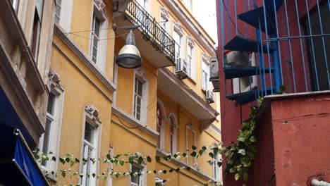 a narrow alleyway with a yellow building on one side and a red building with a blue spiral staircase on the other side