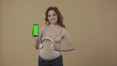 pregnant woman with green screen phone and headphones