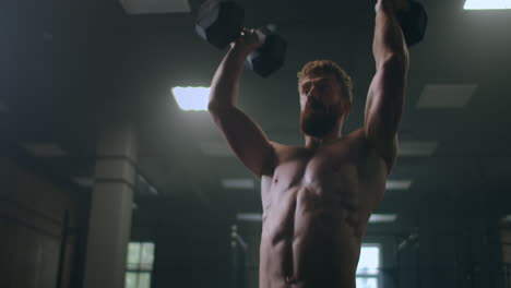 a powerful and strong athlete pushes dumbbells standing in the gym in slow motion.