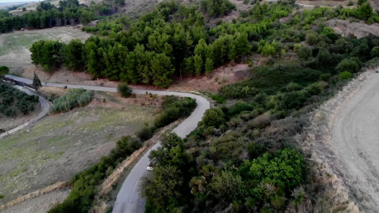 fiat 500 blanco seguido de un dron mientras conduce por la carretera de las colinas en el campo de puglia