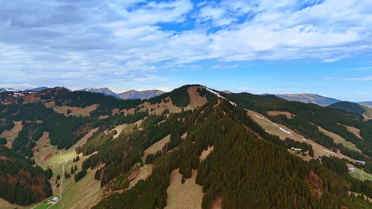 Mountains with wooded areas and bare grassy ones. Rocky background under the cloudy sky. Aerial perspective.