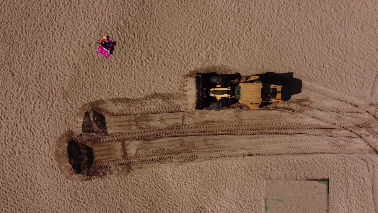 한 사람이 태양에서 휴식을 취하는 동안 해변에서 모래를 가져가는 굴착기