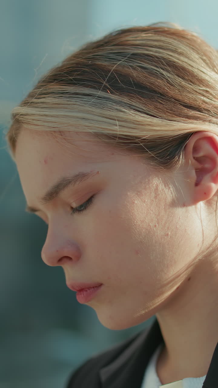Young professional woman with serious expression focused intently on task outdoors near glass building under sunlight, showcasing concentration and determination in urban business environment
